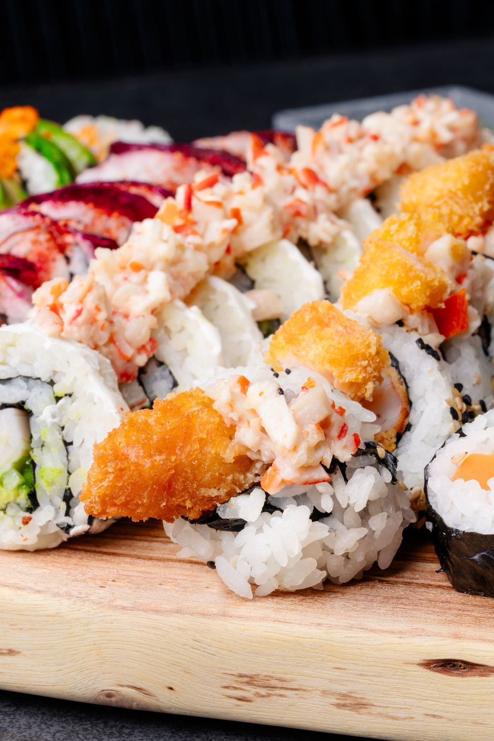 Close-up of fresh sushi rolls with crab meat and tempura on wooden board.