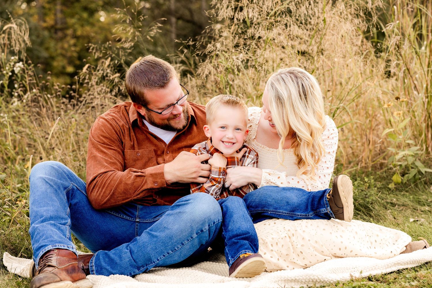Mother lifts baby in joyful moment against golden sunlit trees in park setting.