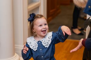 A joyful child in a navy blue dress with white lace collar laughs during a special occasion.