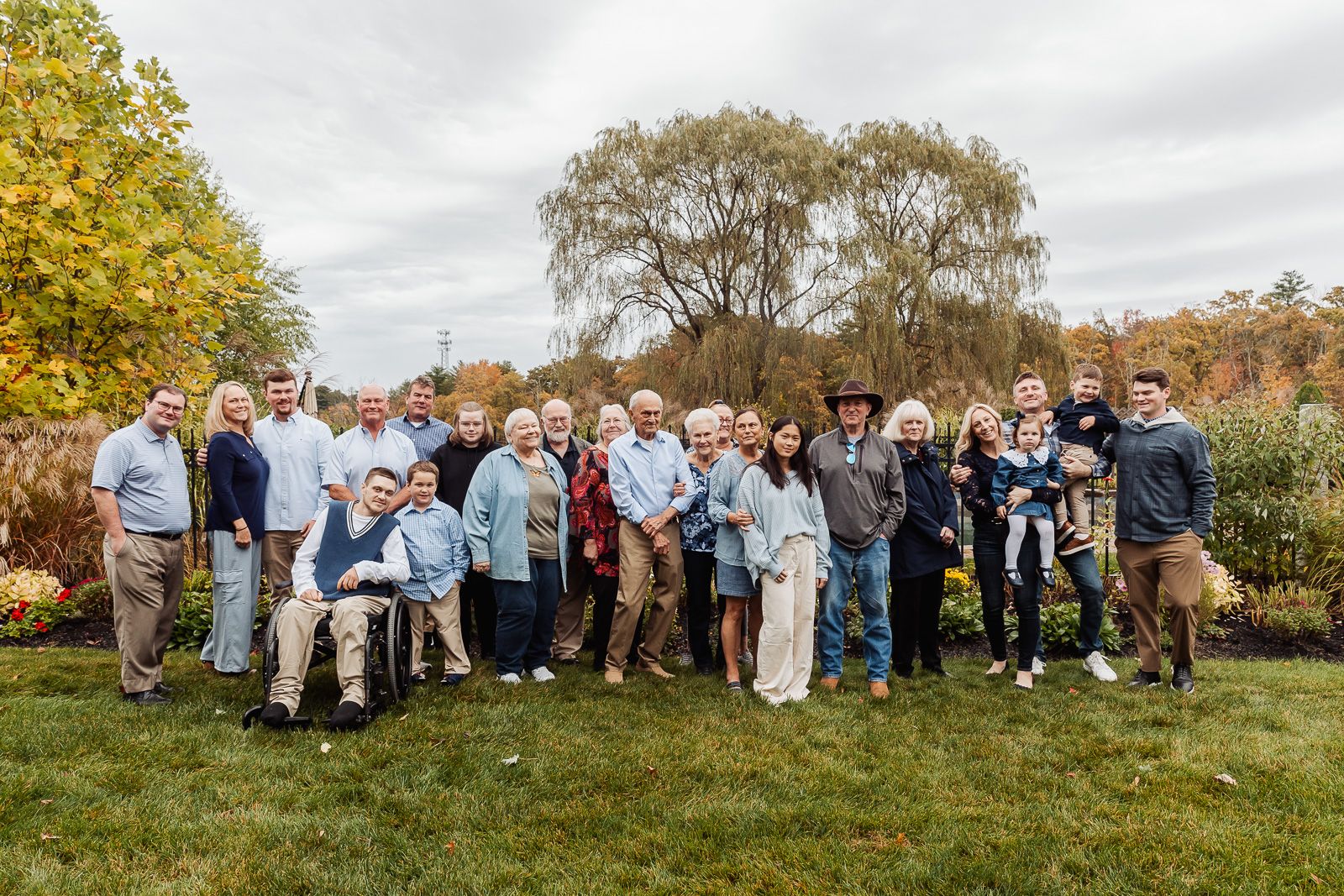 Large multi-generational family group poses together outdoors with autumn trees in background.