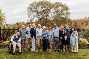 Extended family members gather for group photo in garden with iron fence and willows.