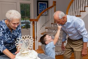 Playful moment shared between generations around decorated white cake by staircase.