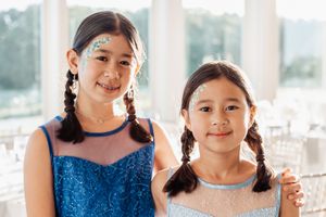 Two young attendees in matching blue dresses and braided hairstyles at a formal event.