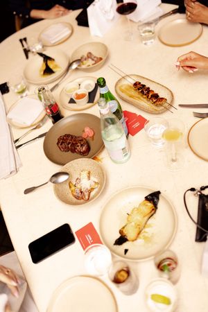 Aerial view of multiple plates with gourmet dishes and beverages on a white dining table.