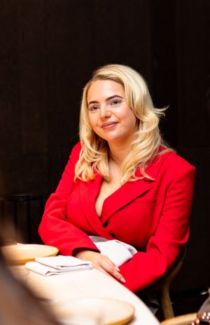 Woman in red blazer seated at dining table with warm lighting.