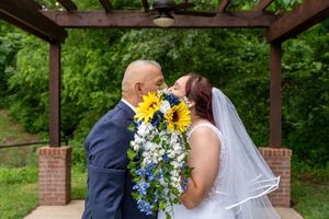 A newly married couple kisses behind her bouquet