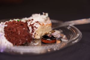 Wedding rings resting on a glass plate beside slices of red velvet and white coconut cake at a reception.