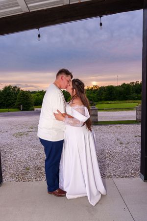 Bride and groom share a romantic kiss at sunset, with the bride in a white gown and groom in blue pants.