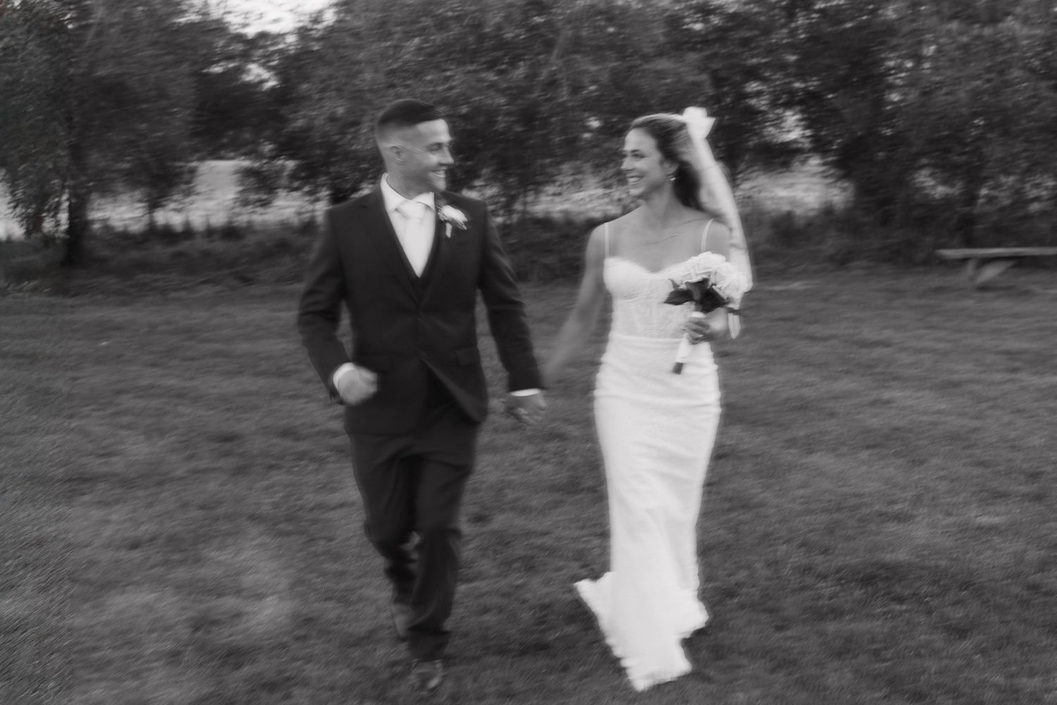 A couple shares an intimate moment on a garden path between white buildings with mountains in the background.