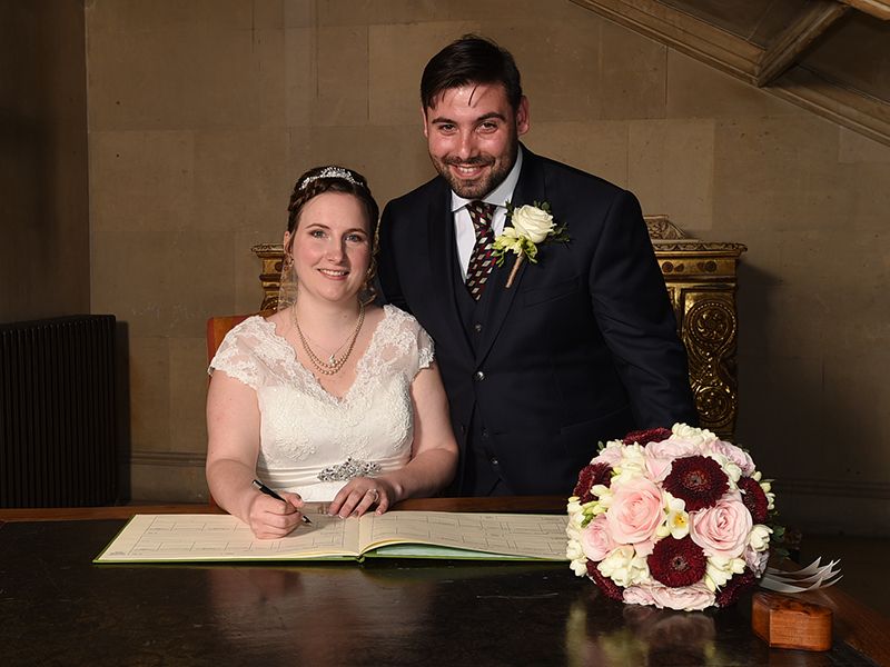 A couple poses for a photo while signing the registrar at Ashridge House, Hertfordshire. Wedding photography captured by Abigail's Studio.