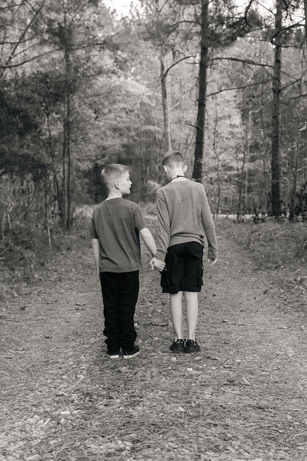 Black and white photo of two people walking together on wooded path.