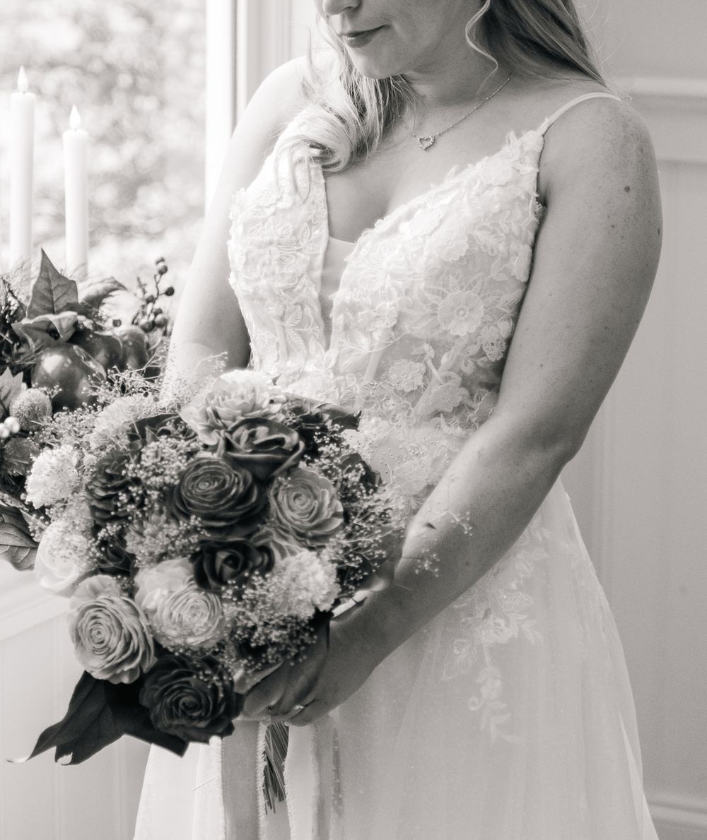 Close-up of bridal bouquet with white and dark roses against white wedding dress.