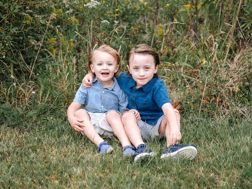 Children sitting together in casual outfits among wildflowers and tall grass.