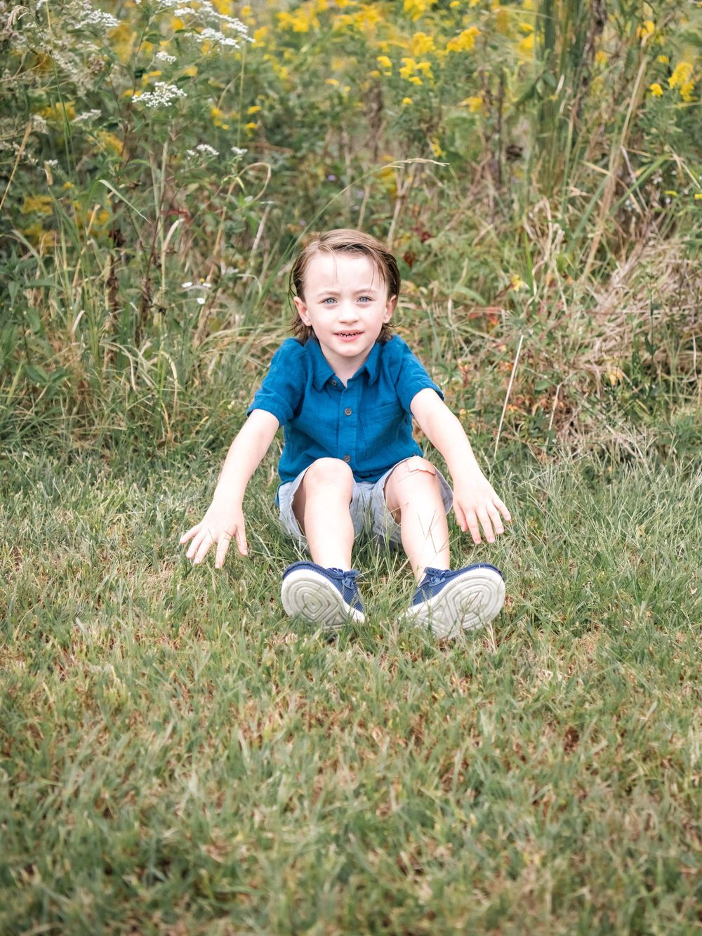 Young child in blue shirt playing outdoors in tall grass with yellow wildflowers.