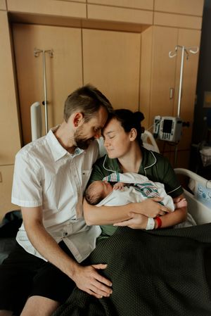 New parents sharing tender moment with newborn baby in hospital room after birth.