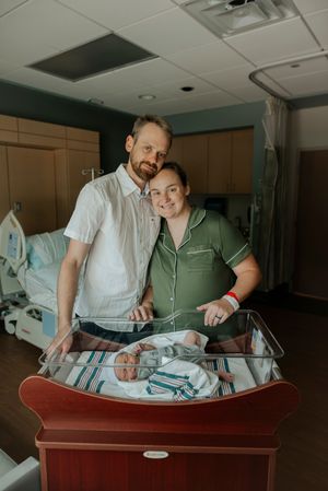 Happy new parents standing beside hospital bassinet with their sleeping newborn baby.