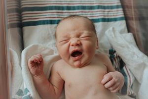 Adorable newborn baby yawning and stretching in hospital bassinet after birth.