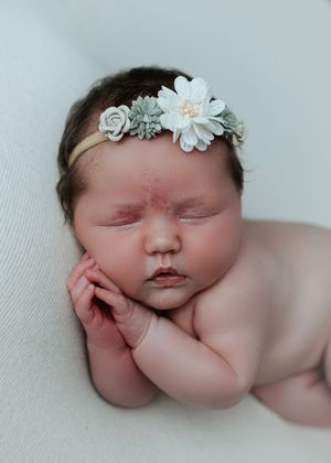 Sleeping newborn baby girl wearing a delicate floral headband with sage green and white flowers.