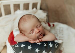 Sleeping newborn baby resting chin on hands atop a star-patterned pillow in a white mini crib. Ivy Lynn Photography, North Georgia