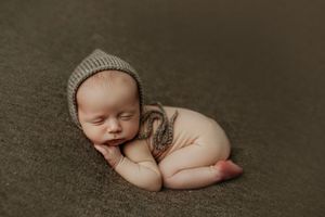 Adorable sleeping newborn baby posed in froggy position wearing a knit bonnet on a green backdrop. Ivy Lynn Photography, North Georgia