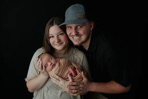 Smiling young couple holding sleeping newborn baby against black studio background.