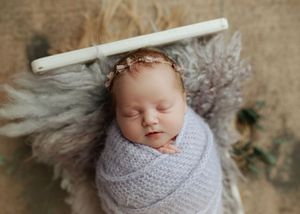 Newborn baby girl wrapped in lavender knit swaddle sleeping in a rustic mini bed prop.