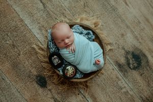 Sleeping newborn wrapped in blue swaddle in round basket with decorative pins.