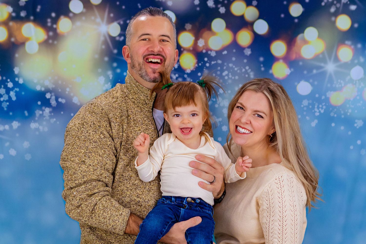Family dressed in cozy sweaters, smiling in front of a beautiful Christmas lights
