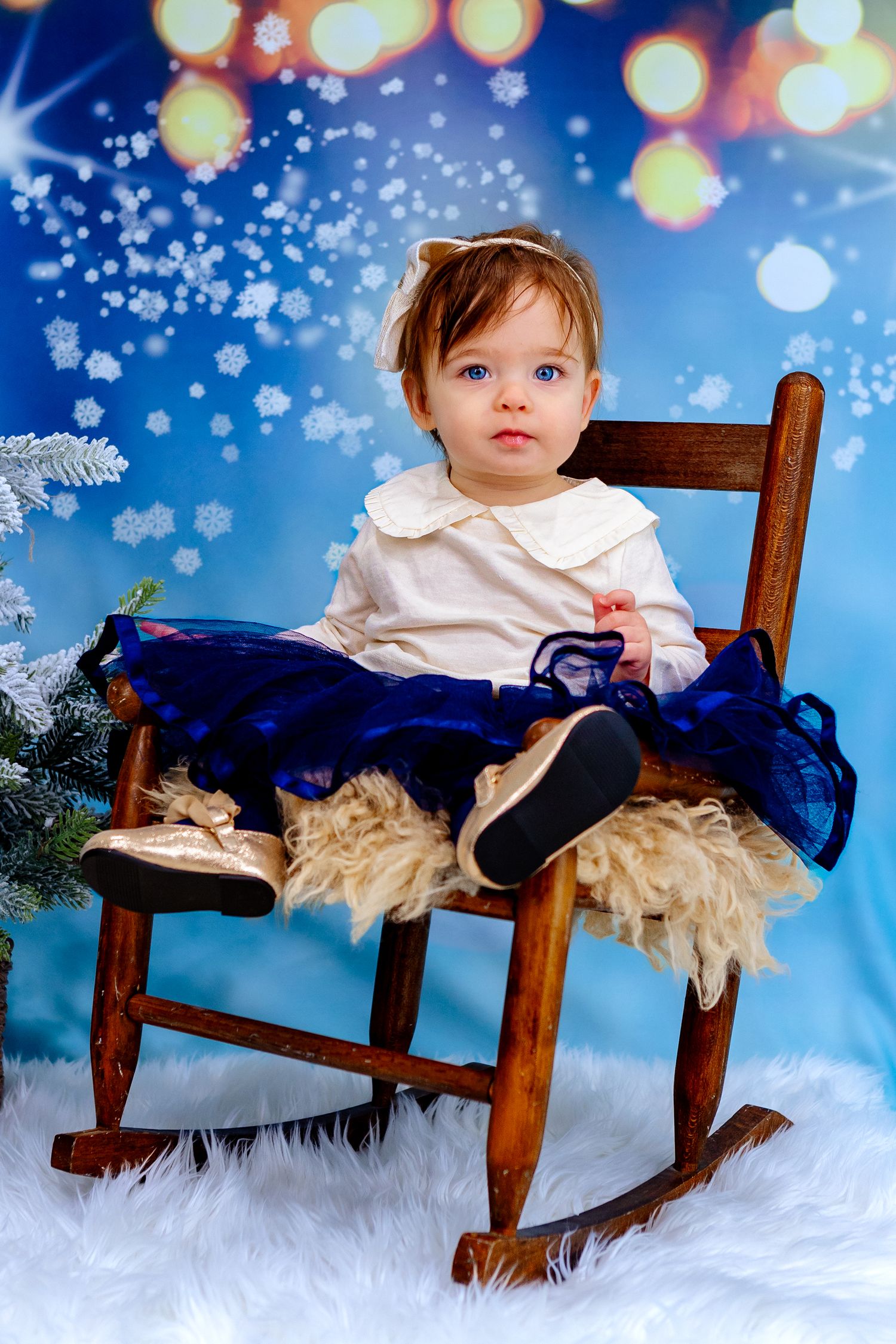 Girl dressed on rocking chair, smiling in front of a beautiful Christmas lights