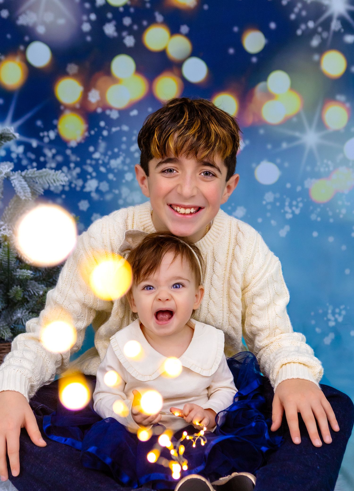 "Siblings in matching Christmas outfit, laughing playing with string of lights