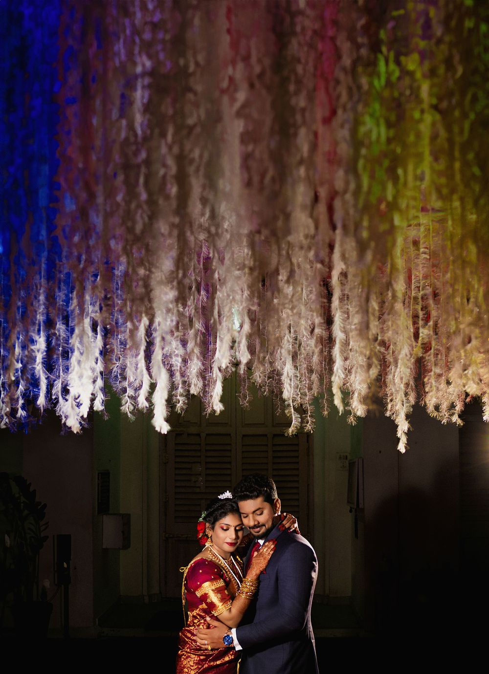 A romantic moment captured under colorful hanging floral decorations at an evening celebration.