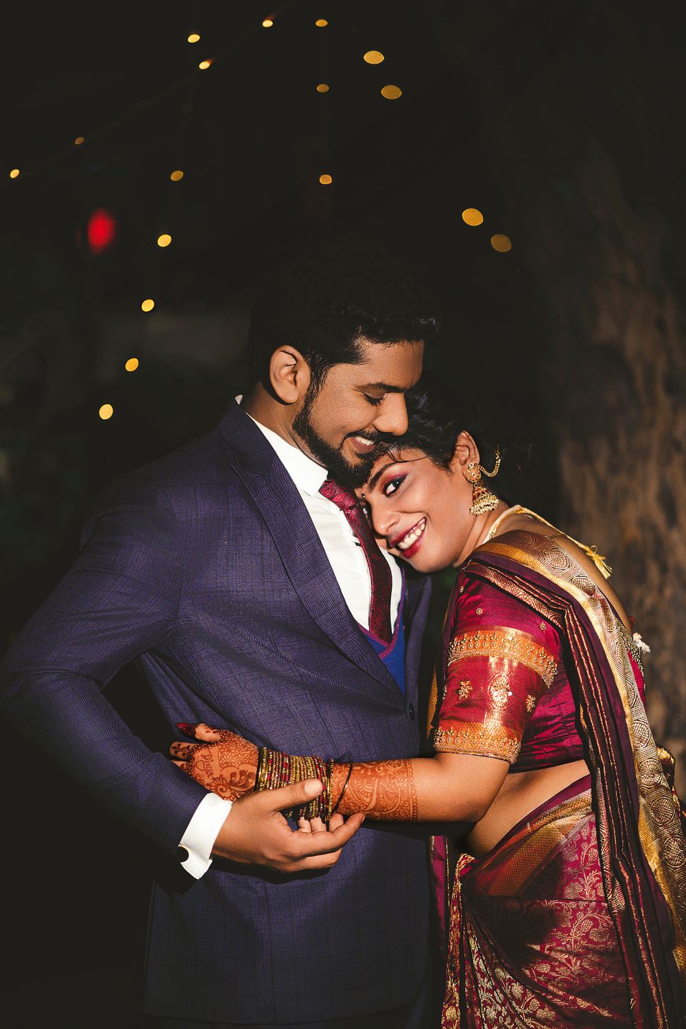 An intimate portrait of a couple in traditional Indian wedding attire under twinkling lights.