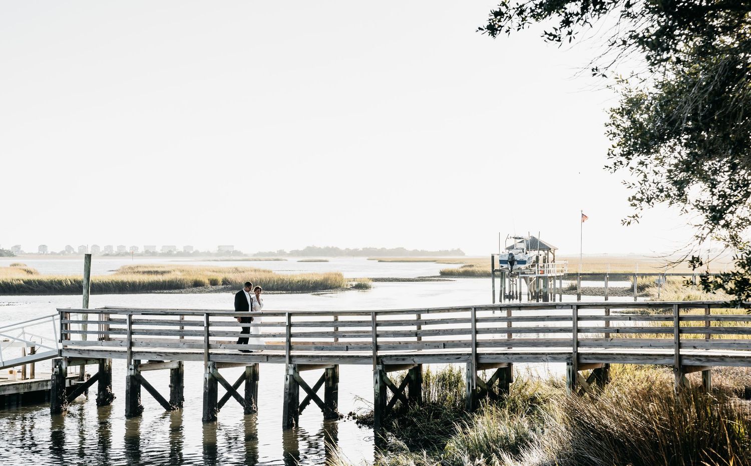 A blonde hair blue eyed girl in a black jumpsuit poses under string lights leaning against a railing