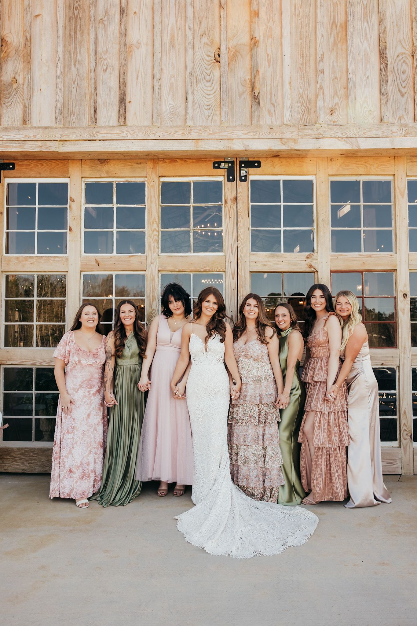 bride with her bridal party posing in front of glass garage doors. They are wearing pinks/greens/floral dresses
