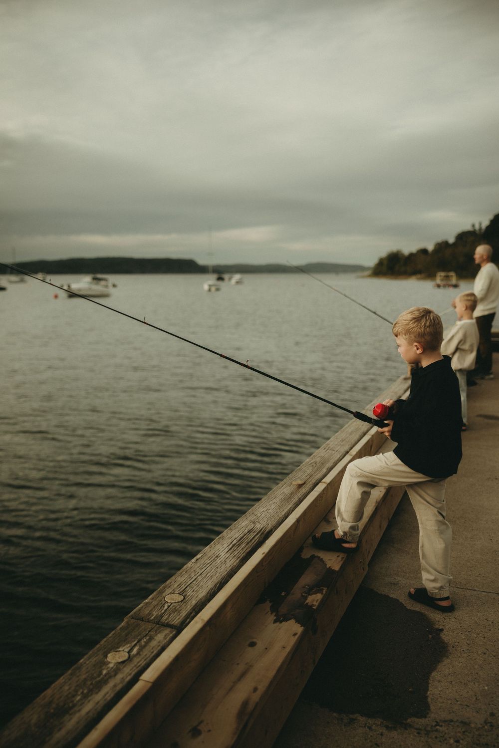 Young anglers sitting on dock edge with fishing rods over calm water.