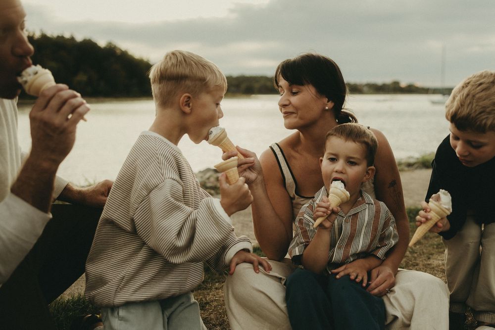 A joyful group gathering on a beach at sunset sharing ice cream cones together.