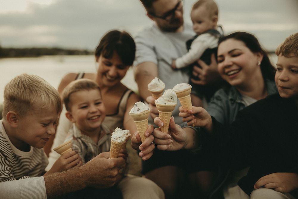 Friends laughing and eating ice cream cones while sitting outdoors by the water.