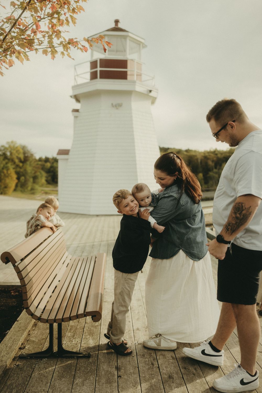 A family shares an embrace near a white lighthouse on a wooden boardwalk.