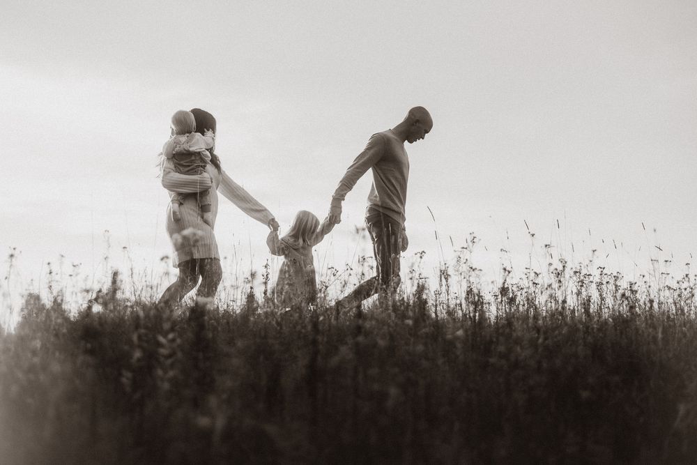 Family and dog playing together in a tall grass field at sunset.