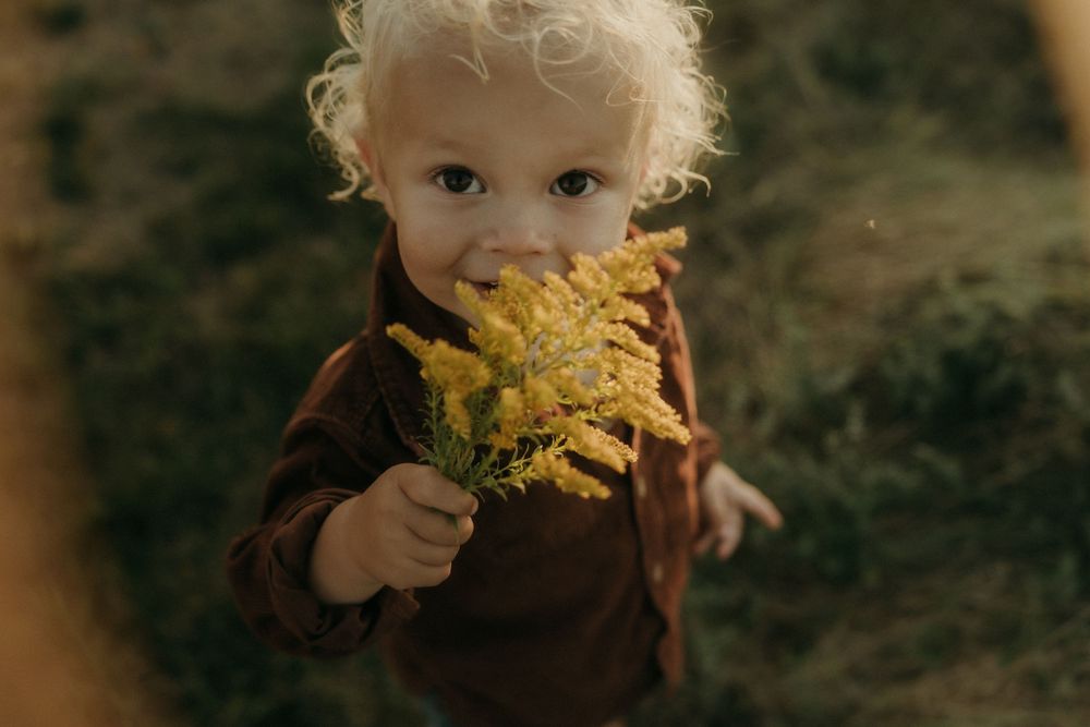 A young child with blonde hair enjoys snacks outdoors in natural lighting.