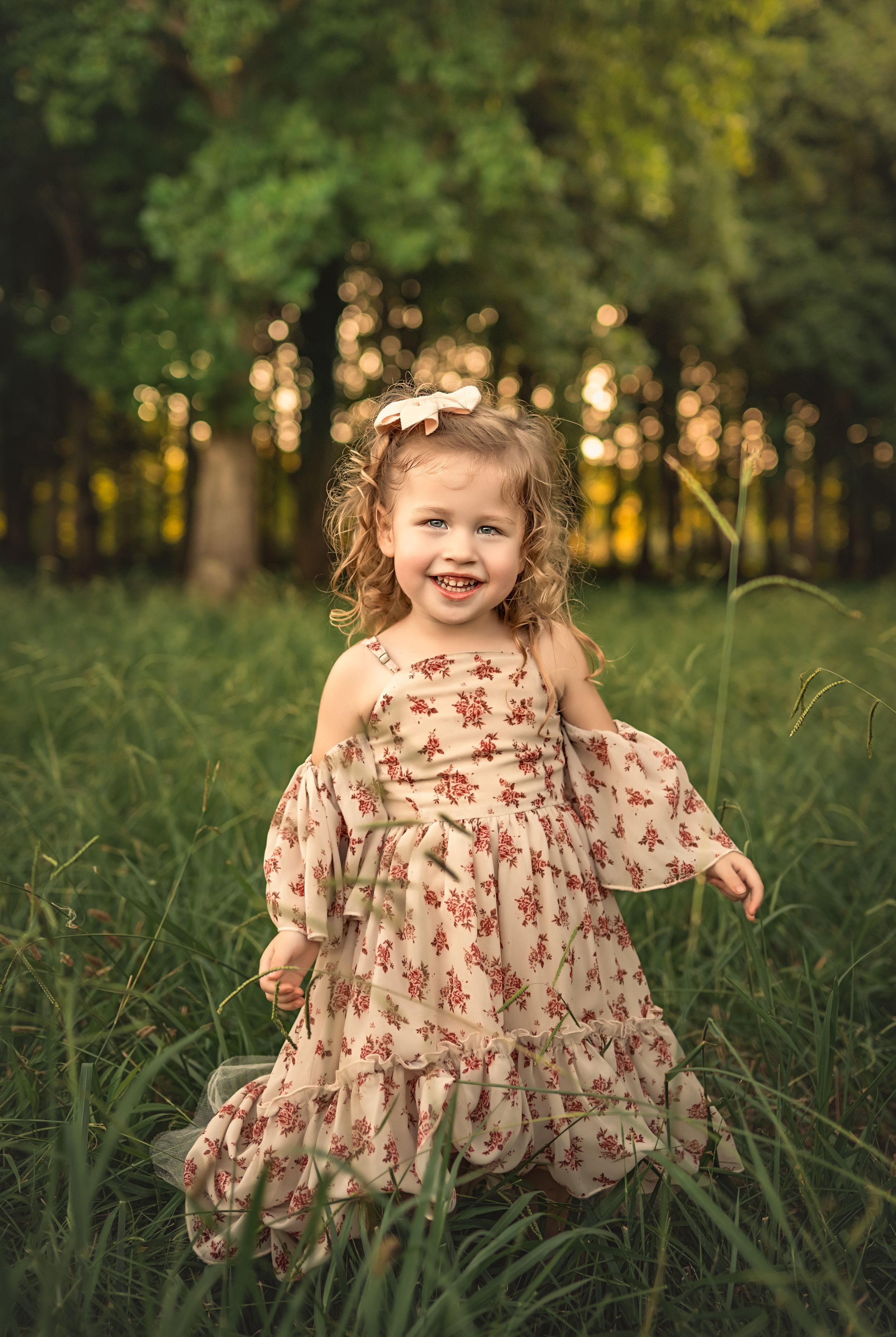 A young child wearing a floral dress twirls playfully in a grassy field during golden hour.