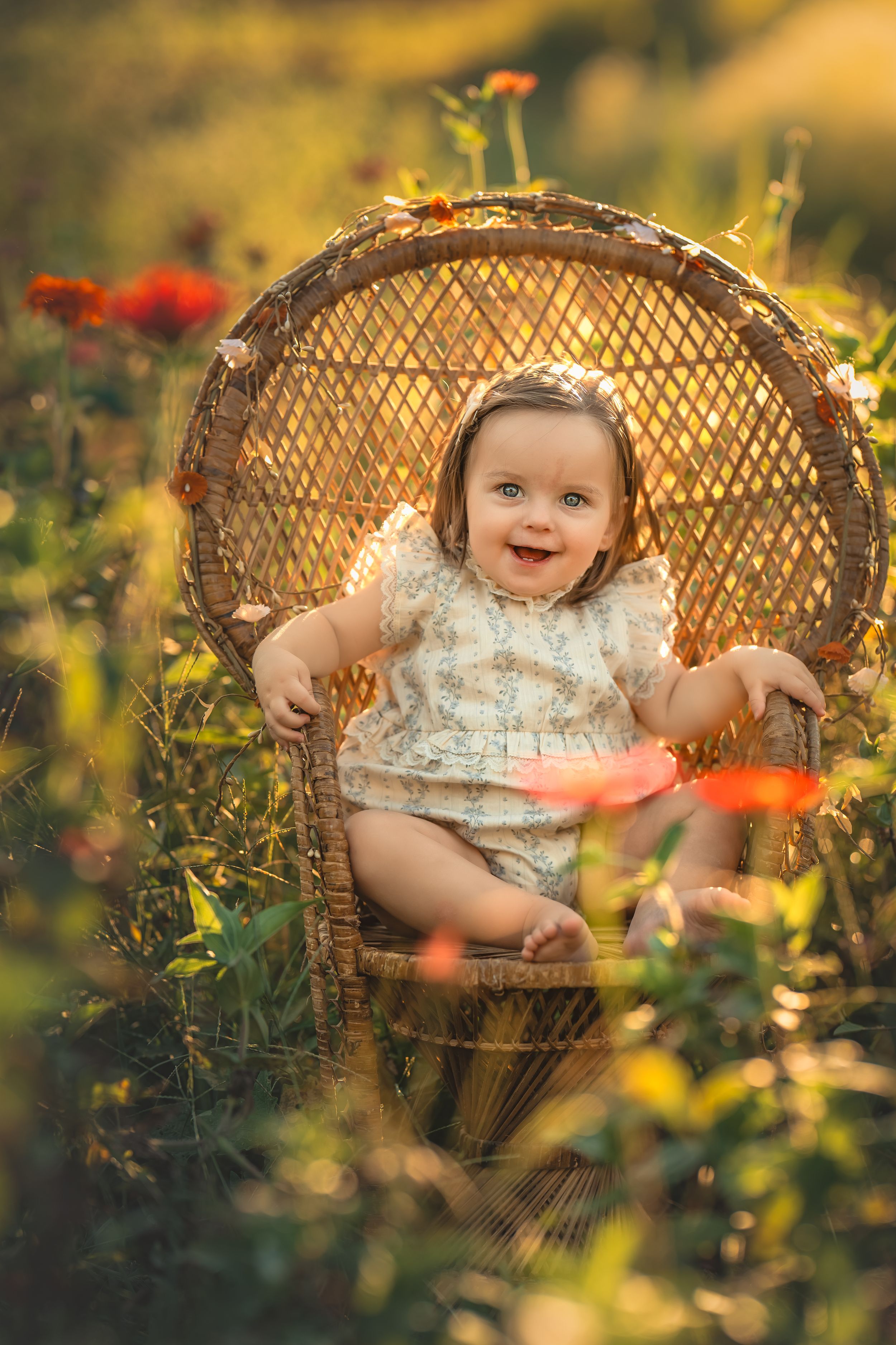 A baby girl sits in a child's wicker peacock chair surrounded by vibrant wildflowers for dreamy photos with Atlanta Children's photographer.