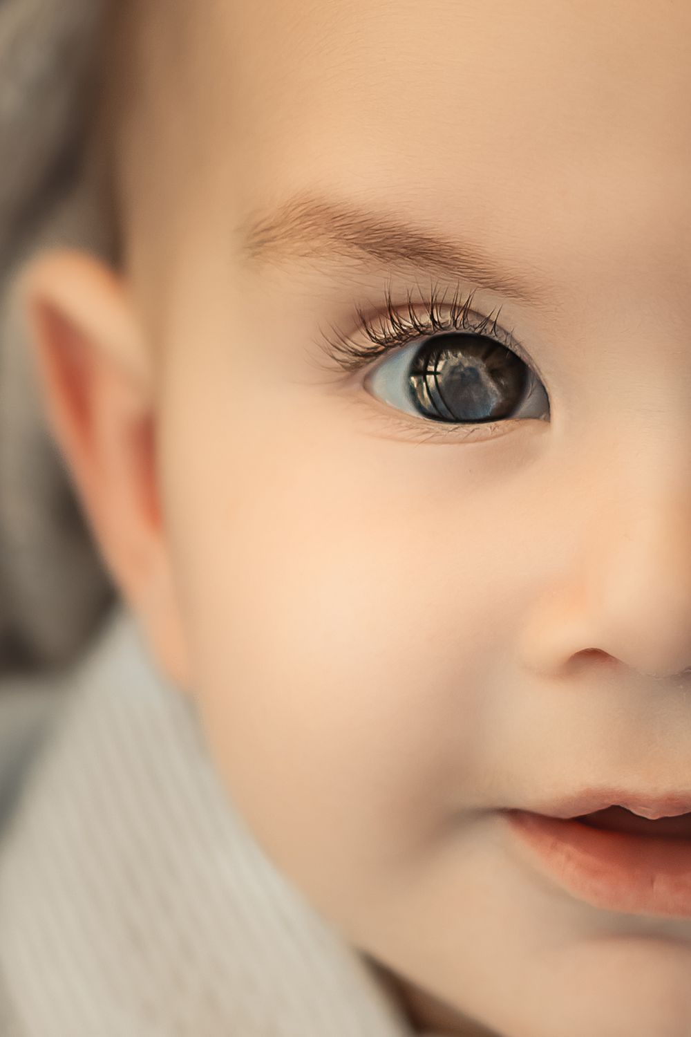 Extreme close up macro photo of a baby boy showing half the face of sweet baby cheeks and red rosy lips with big eyes.