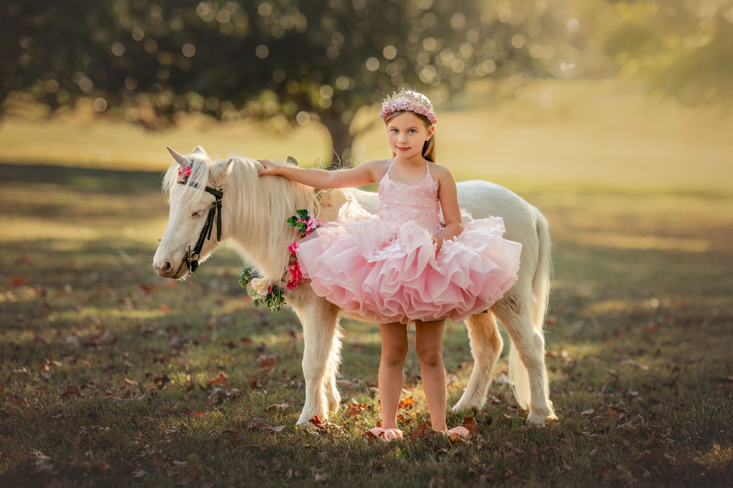 6-year-old girl in pink tutu dress and crown poses with a white pony for unicorn photo session with Atlanta Children's Photographer.