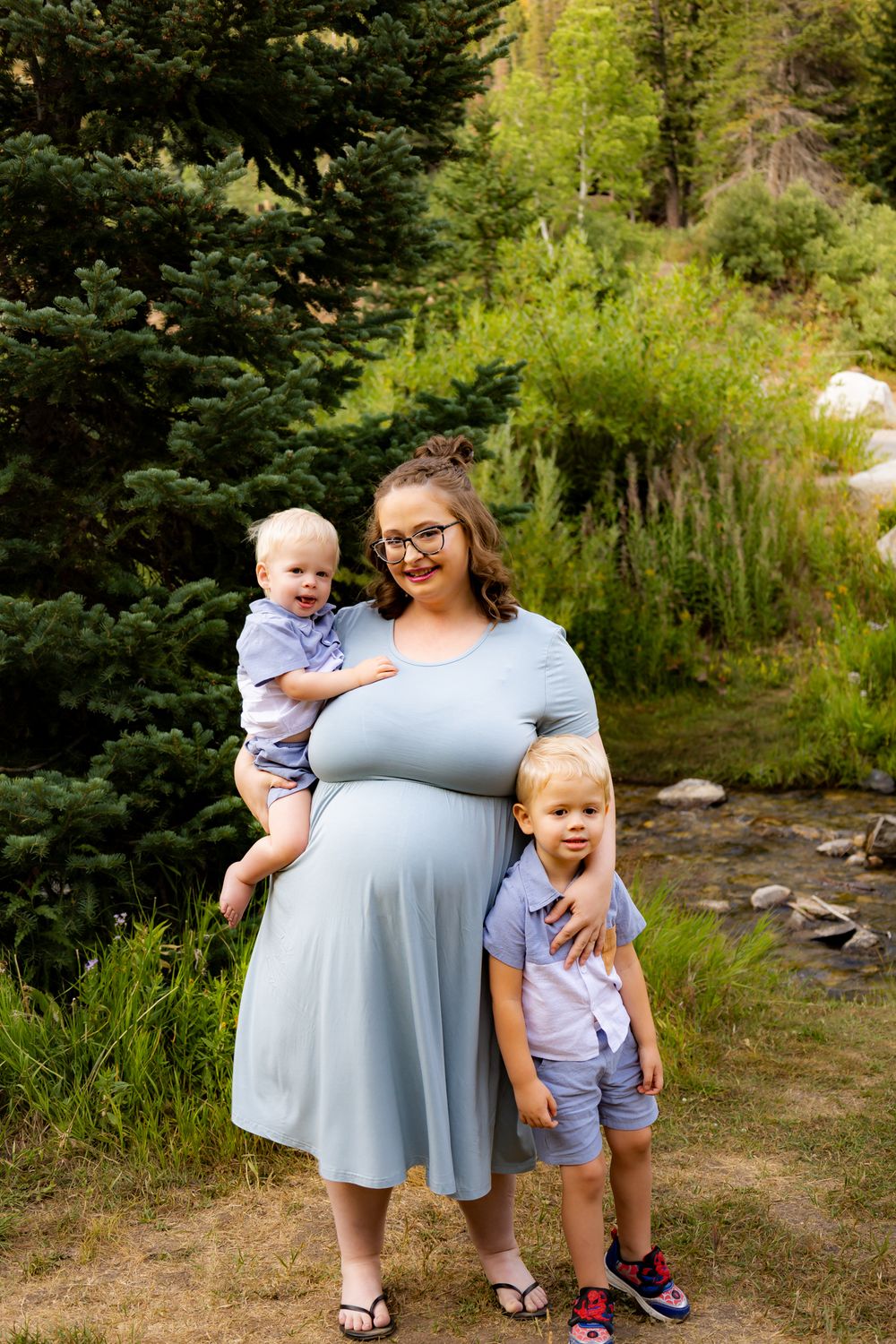Family portrait in a natural outdoor setting with pine trees and mountain scenery.