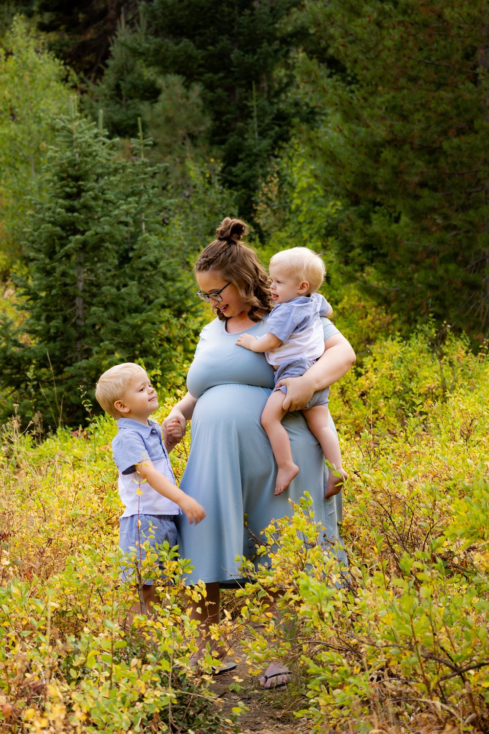 Family candid moment captured in mountain meadow with yellow wildflowers and evergreen trees.