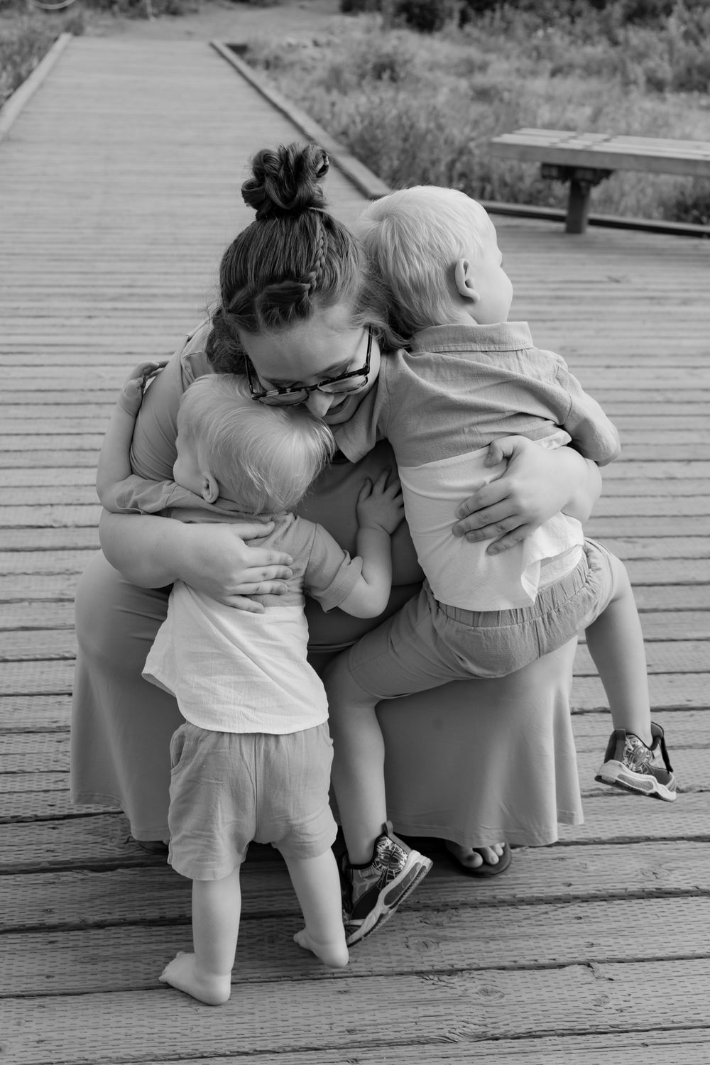 Black and white capture of intimate family embrace on wooden deck.