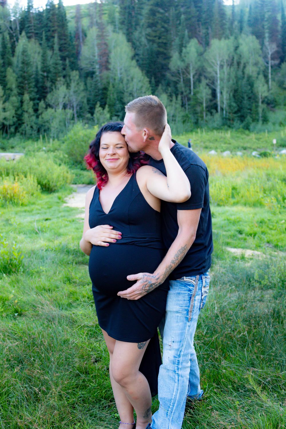 Romantic couple poses together in a mountain meadow surrounded by pine trees and summer flowers.