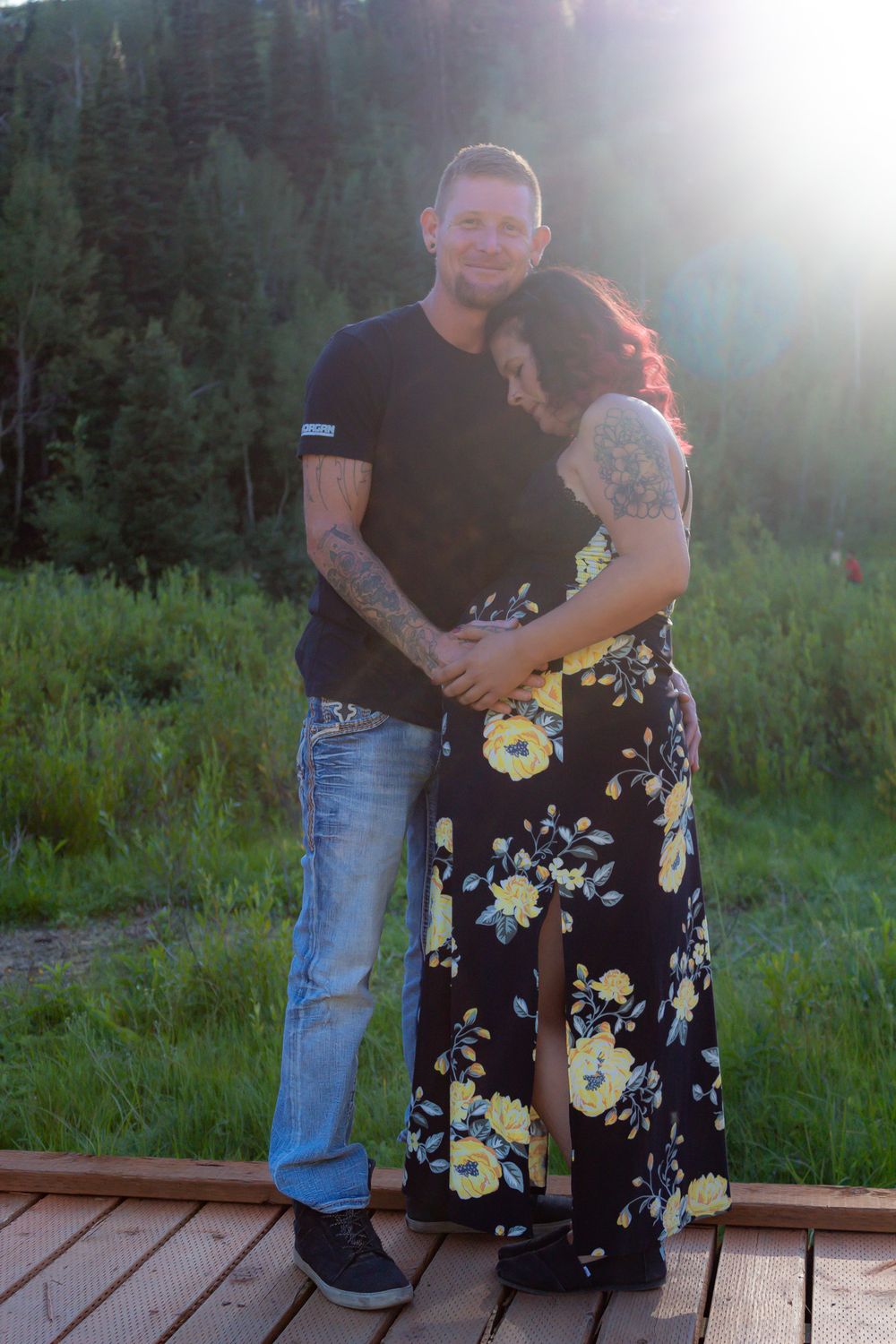 Couple embracing on wooden deck with dramatic sunset lighting and mountain views.