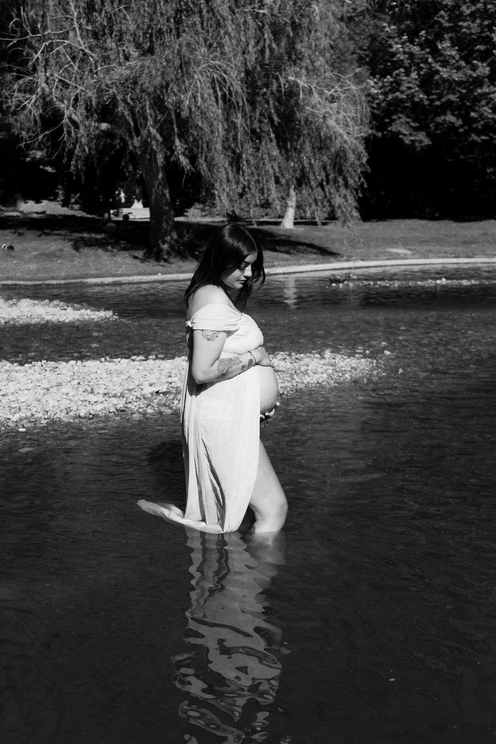 Black and white photos of two people embracing in shallow water near a wooded shoreline.